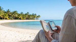 Personne sur une plage mauricienne lisant un guide « Mauritius Explorer » et consultant une carte de l'île sur smartphone.