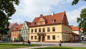 Rue historique de Toruń : maisons colorées aux toits rouges, bâtiment jaune central, banc avec personnes au premier plan sous ciel bleu.
