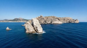 Iles Medes: îlots rocheux blancs dans une mer bleue, avec un phare sur la plus grande île et une côte montagneuse en arrière-plan.