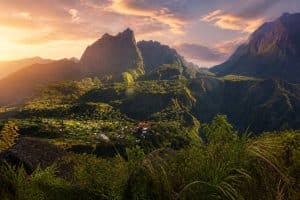 Un village niché au cœur d'un cirque montagneux verdoyant sous un ciel orangé au lever du soleil à La Réunion.