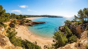 Vue panoramique d'une crique isolée aux eaux turquoise à Salou, entourée de falaises rocheuses et de pins.