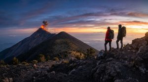 Deux randonneurs équipés de sacs à dos regardent le volcan Fuego en éruption au coucher du soleil depuis l'Acatenango.